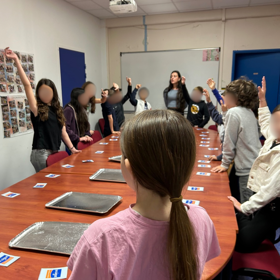 enfants debouts autour d'une table et levant la main